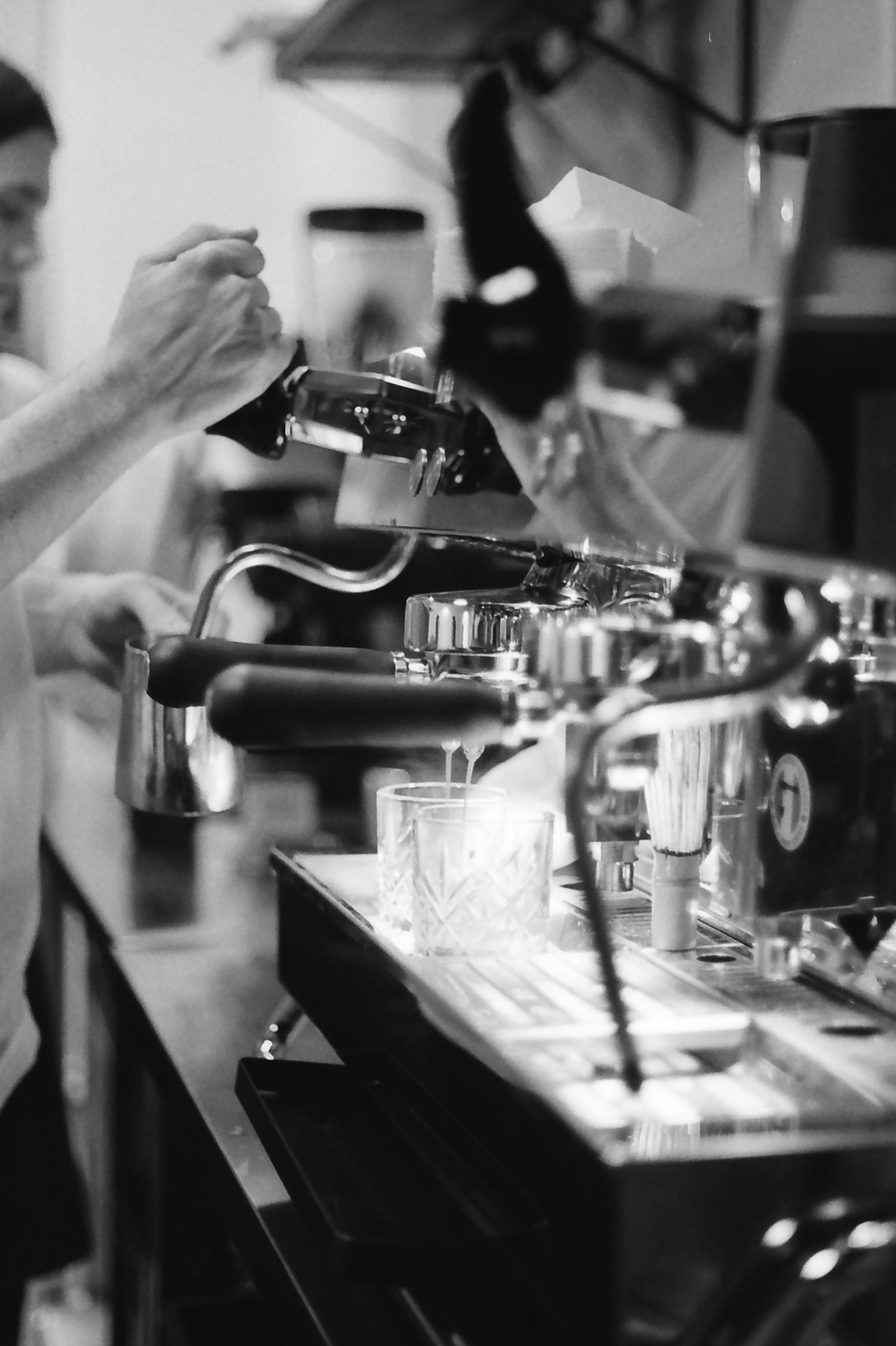 Hände an der Siebträgermaschine, Espresso läuft in ein Glas, Schwarzweißfoto